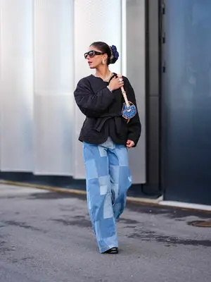 Woman wearing patchwork jeans, black quilted jacket, shoulder bag, sunglasses, scrunchie, and black shoes