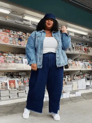 Nnenna Echem wears a light blue button-down shirt, light wash loose jeans, denim handbag, and silver flats