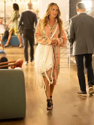 Sarah Jessica Parker as Carrie Bradshaw wears a patterned button-down dress, black gladiator sandals, and white fringe handbag
