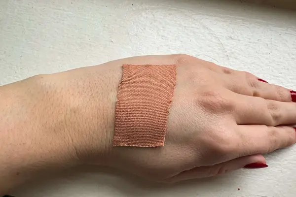 A person wears a piece of VBT Breast Tape on the back of their hand