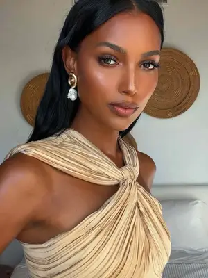 Jasmine Tookes wearing gold and silver earrings and gold twisted top
