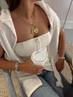 model wearing two long pendant gold necklaces, holding cup of coffee