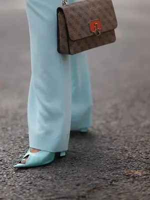 Close-up of person wearing blue peep-toe heels, pants, and logo-covered Gucci handbag