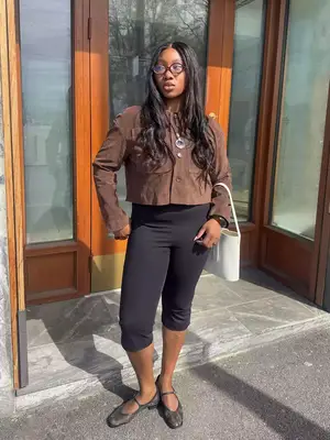 A person wearing a knit sweater and pleated skirt, their hand on their hip