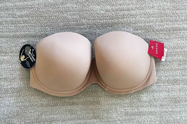 Spanx Up For Anything Strapless Bra with tags displayed on a beige carpet background 