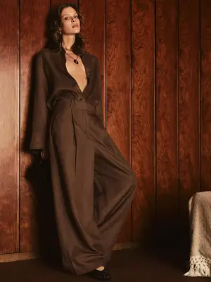 Woman wearing brown open blouse, wide leg trousers, and layered necklaces