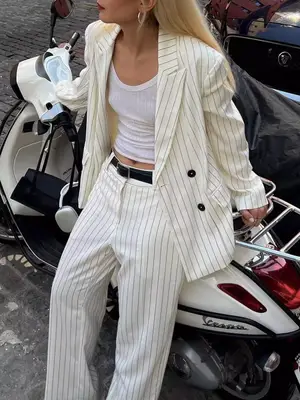 Woman wearing ribbed tank top and pinstriped white suit while standing against Vespa