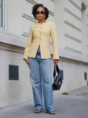 woman wearing a yellow button-down top and jeans with black strappy heels and handbag