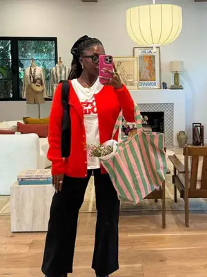 Toni Bravo wearing a red cardigan, black wide leg pants, and white graphic tee and posing for a mirror selfie