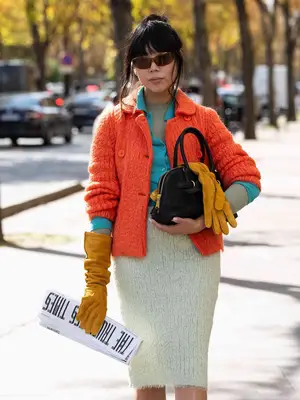 Susie Lau wears an orange cardigan over a teal cardigan and a gray top and textured skirt