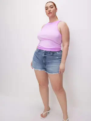 Model wearing denim shorts, pink tank top, and white heeled thong flip flop sandals