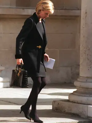 Princess Diana wearing all-black outfit featuring dress, coat, tights, pumps, and handbag