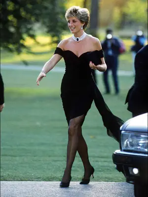 Princess Diana wearing iconic revenge dress, walking outside wearing black dress draped over shoulders with statement necklace, black tights, and black heels
