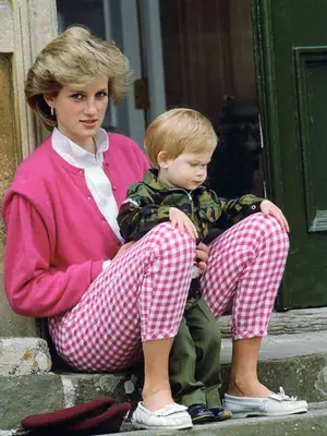 Princess Diana sitting on ground with Prince Harry sitting in lap. She