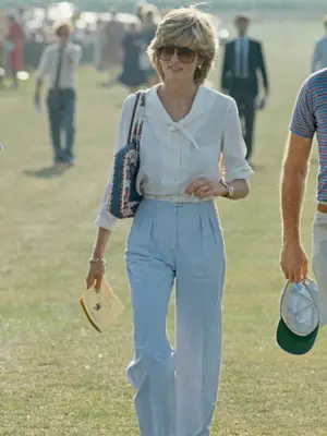 Princess Diana wears sunglasses, quilted shoulder bag, white button-down, and blue striped slacks