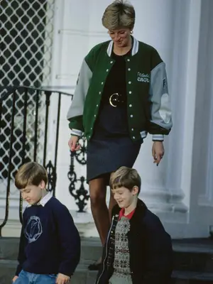 Princess Diana wearing Philadelphia Eagles varsity jacket, black shirt, and belted pencil skirt while walking outside with Prince William and friend