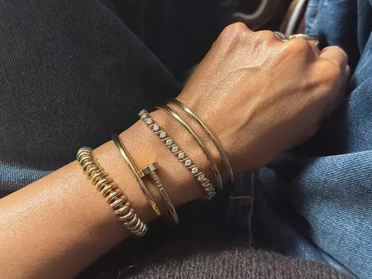 Close-up of woman wearing stacked gold and gem bangles and bracelets, styled with jeans
