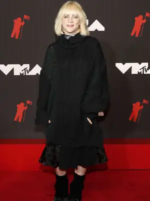 Billie Eilish wears a black sweater dress, midi skirt, and boots to the 2021 MTV Video Music Awards