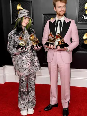Billie Eilish and Finneas wear pink, gray, and black Gucci outfits and hold their 2021 Grammy Awards
