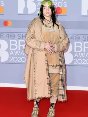 Billie Eilish wears a Burberry trenchcoat, shorts set, socks, sneakers, and bonnet to the 2020 Brit Awards