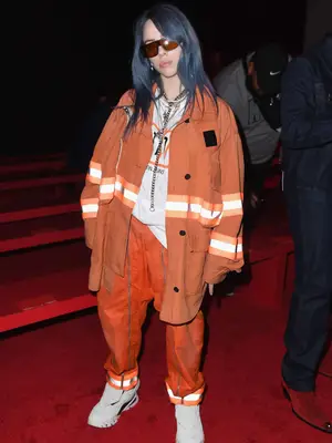 Billie Eilish wears a Calvin Klein caution tape jacket, t-shirt, and utility pants to the brand
