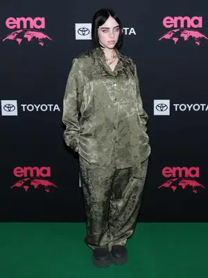 Billie Eilish wears green floral silk Gucci pajamas, layered necklaces, and black lug sole boots