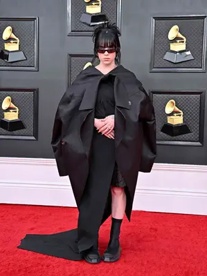 Billie Eilish wears a black caped Rick Owens gown, platform flat boots, and sunglasses to the 2022 Grammys