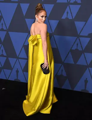 J.Lo wears a strapless yellow Reem Acra column gown with a back bow to the 2019 Academy Governors Awards