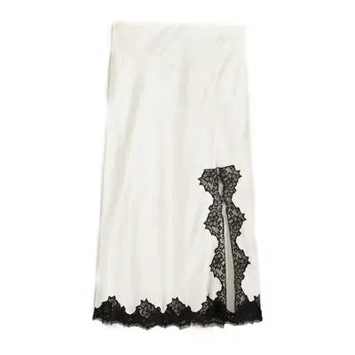 A person wearing black and gold toe ring sandals, with hands rested on lap showcasing rings