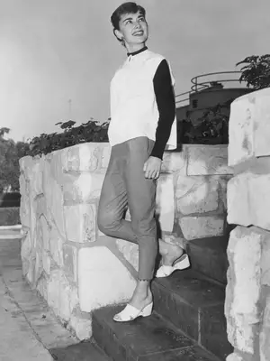 Audrey Hepburn wearing a white top with a black long sleeve shirt, cropped pants, and open-toe wedges