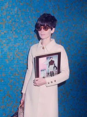 Audrey Hepburn in a camel-colored coat with brown sunglasses and a croc purse