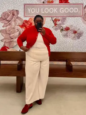 Abisola Omole wears cream trousers, a cream top, and red cardigan