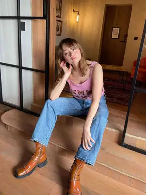 Aimee Lou Wood wearing a pink tank top, jeans, and square-toe boots