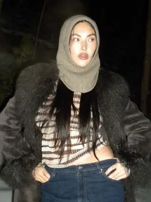 Yumi Nu wears a knit balaclava, striped sweater, and fur-trim coat