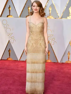 Emma Stone wears a gold Givenchy gown with embroidery, lace, and fringe detailing to the 2017 Oscars
