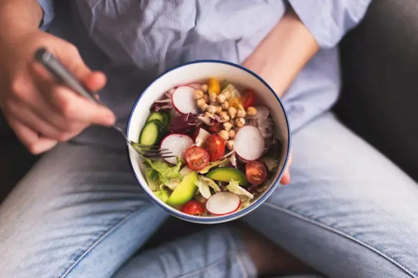 Green vegan breakfast meal in bowl with spinach, arugula, avocado, seeds and sprouts. Girl in leggins holding plate with hands visible, top view. Clean eating, dieting, vegan food concept
