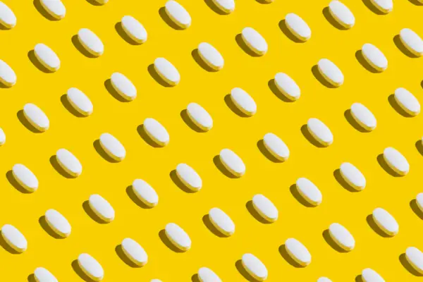 White pills on yellow background. Minimal medical concept. Pharmaceutical, Covid-19 or Coronavirus. Flat lay, top view