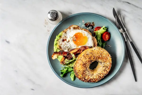 Bagel sandwich with avocado, fried egg and side salad on white background