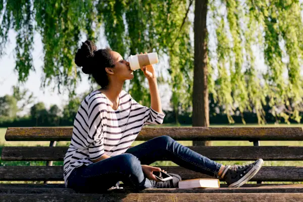 Young woman sitting on park bench drinking coffee to go
