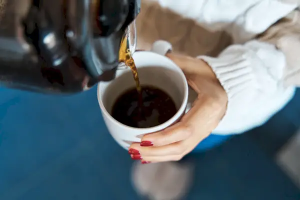 Woman pouring herself hot coffee to a mug.