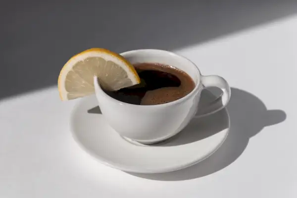 Coffee cup with espresso served with lemon on white background with shadows and sunlight