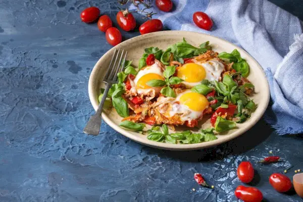 Piatti tradizionali della cucina israeliana Shakshuka Uovo fritto con verdure, pomodori e paprika in un piatto di ceramica con stoffa, erbe e ingredienti sopra su sfondo texture blu Copia spazio
