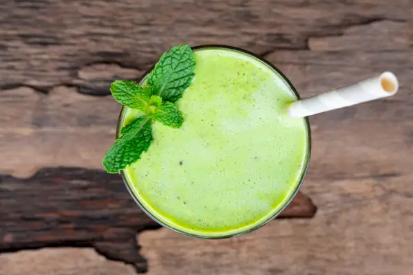Frullato di succo di frutta allo yogurt kiwi e succo di kiwi verde bevono un gusto sano e delizioso in un bicchiere per dimagrire su uno sfondo di legno bianco dalla vista dall'alto.