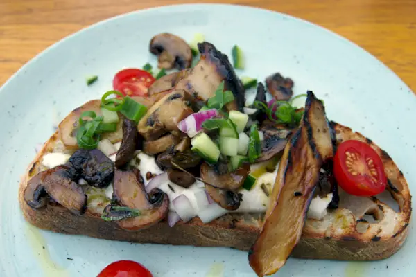 king brown e funghi champignon con formaggio di capra, salsa al dragoncello, pomodorini e olio al tartufo su pane tostato a lievitazione naturale