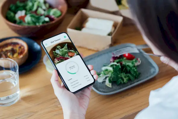 Young Woman Counting Calories With Smartphone While Eating