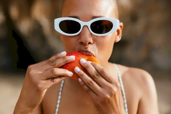 Woman wearing sunglasses eating mango at beach