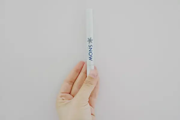 A hand holding a single Snow Teeth Whitening stick