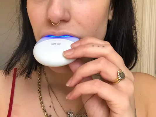 Person holding the Crest 3D White Whitestrips with Light in their mouth 