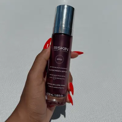 A hand holding a bottle of 111Skin sunscreen