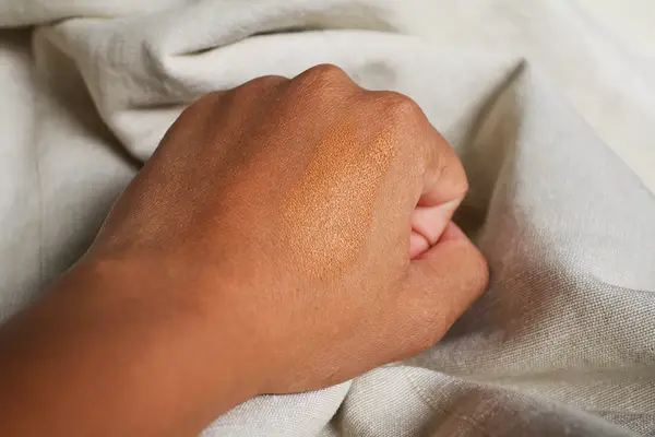 Closed fist with Bobbi Brown Skin Foundation Stick on the back of it 